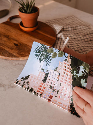 Carnet de notes Positano Mimi & August, carnet qui représente des immeubles orangés avec des arbres. Fait à Montréal, parfaite idée de cadeau pour femme.
